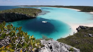 Un paisaje costero con aguas turquesas cristalinas, una playa de arena y afloramientos rocosos.