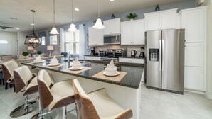A modern kitchen with white cabinets, stainless steel appliances, and a central island with bar stools. - Westside Triumph | Corner Lot With No Rear Neighbors with Loft & Game Room (Kissimmee)
