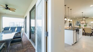 A modern kitchen with a central island, pendant lighting, and a dining area with a glass door leading to an outdoor patio. - Westside Triumph | Corner Lot With No Rear Neighbors with Loft & Game Room (Kissimmee)