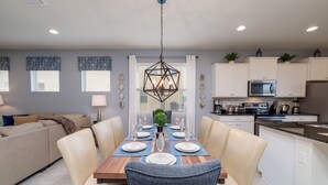 A modern dining area with a wooden table set for six, surrounded by cream-colored chairs. - Westside Triumph | Corner Lot With No Rear Neighbors with Loft & Game Room (Kissimmee)