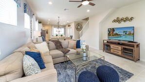 A modern living room with a beige sectional sofa, a glass coffee table, and a TV on a wooden stand. - Westside Triumph | Corner Lot With No Rear Neighbors with Loft & Game Room (Kissimmee)