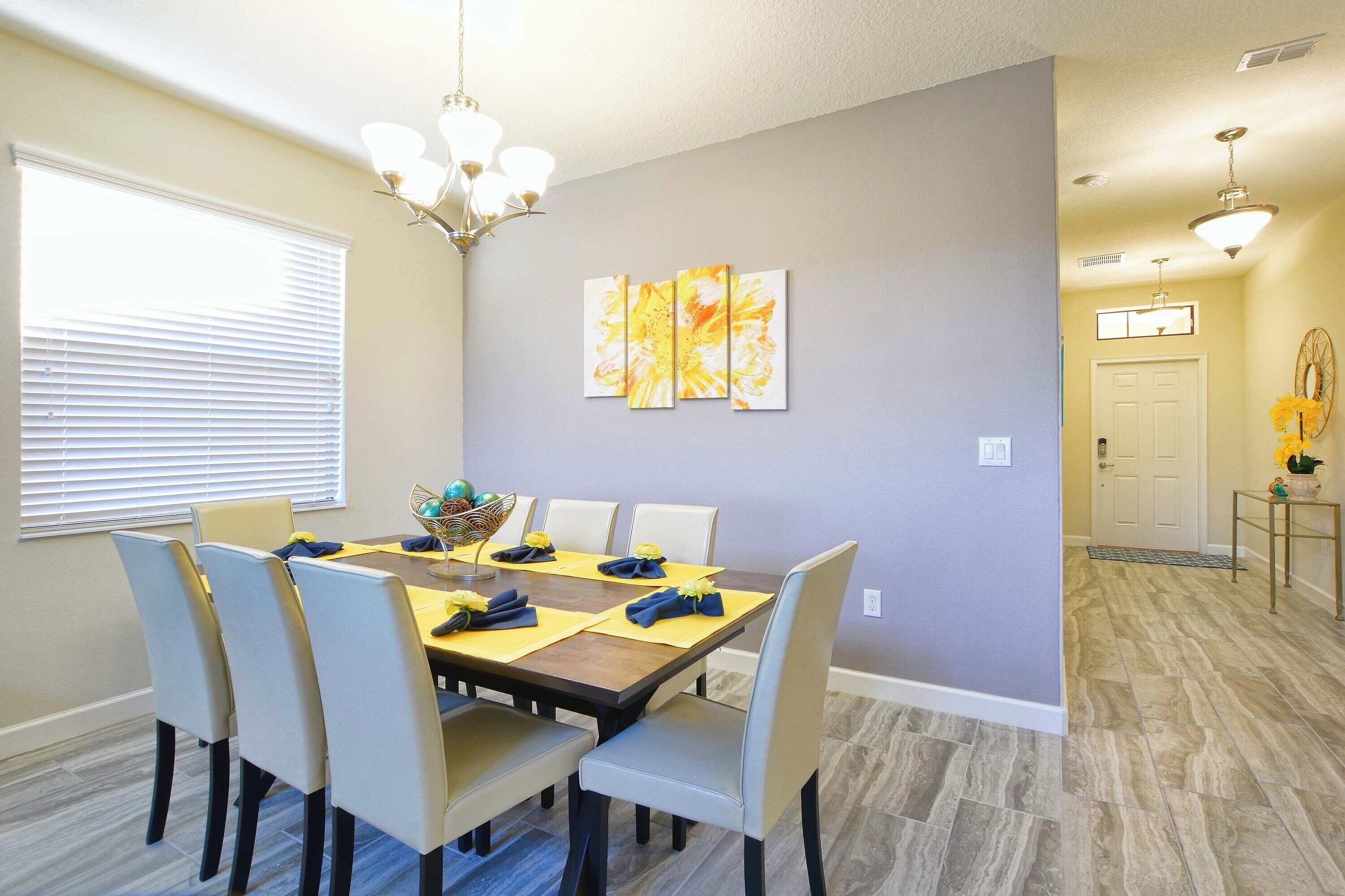 A dining area with a table set for six, chairs, a chandelier, and wall art.