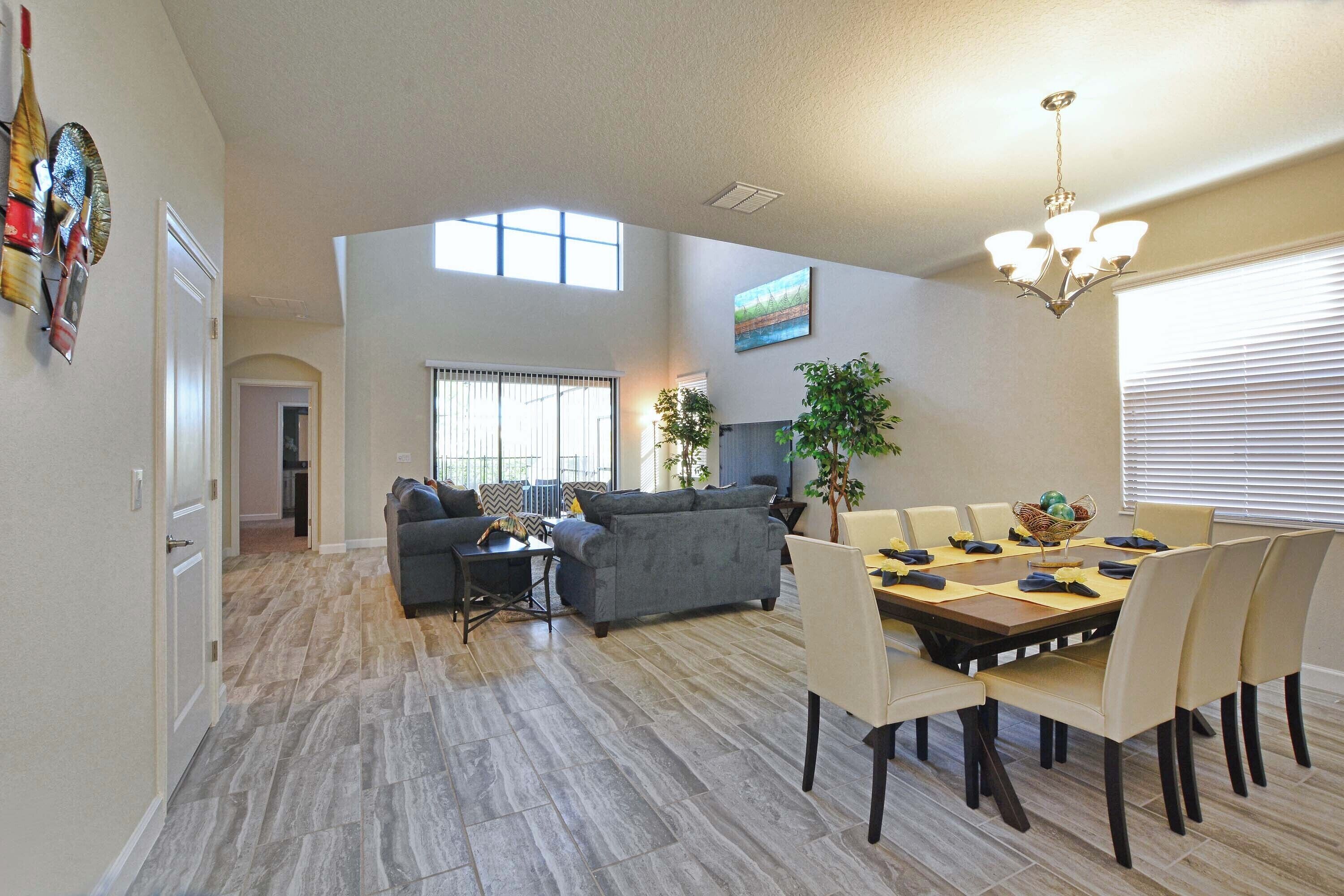 A spacious living area with a dining table, sofas, and a chandelier.