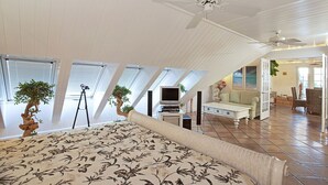 Un amplio dormitorio en el ático con una cama grande, un ventilador de techo y una televisión.