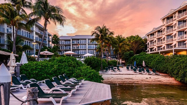 Un resort con un muelle de madera, sillas de descanso y una zona de playa.