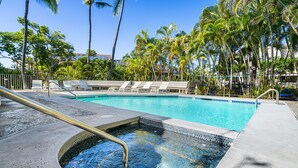 Una piscina con idromassaggio, circondata da palme e lettini.