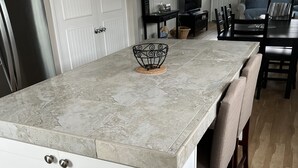Una cocina con encimera de mármol, armarios blancos y un comedor con sillas y mesa.