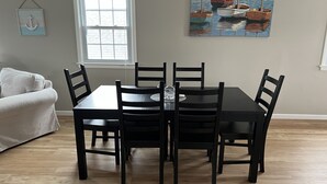 A dining area with a rectangular table and four chairs, a white couch, a window, and a painting on the wall. - Spacious 2nd floor Condo with Two Large Balconies! (Ocean City)