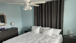 A bedroom with a bed, a nightstand, a bedside table, a mirror, and a ceiling fan. - Spacious 2nd floor Condo with Two Large Balconies! (Ocean City)