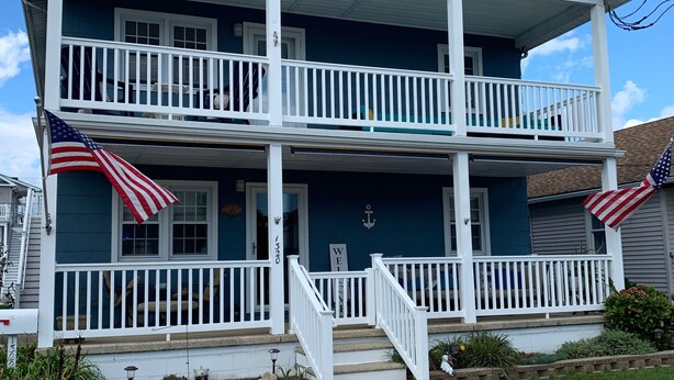 A two-story house with a front porch, a small garden, and two American flags. - Spacious 2nd floor Condo with Two Large Balconies! (Ocean City)