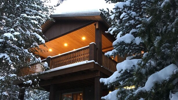 Una cabaña de madera con balcón, rodeada de árboles cubiertos de nieve.