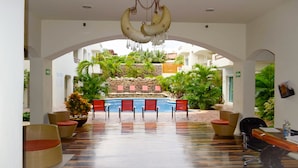 A hotel lobby with a pool, red lounge chairs, and a ceiling with hanging banana-shaped decorations.