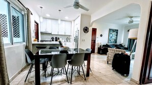 A modern kitchen with white cabinets, a dining table with chairs, a ceiling fan, and a kitchen island with a fruit bowl.