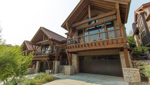 Une maison en bois à deux étages, dotée d’un balcon, de piliers en pierre et d’un garage.
