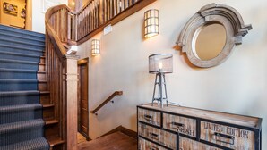 Un escalier en bois avec une rampe, un grand miroir rond fixé au mur et une commode de style ancien dotée de tiroirs.