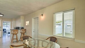 A dining area with a glass-top table and wicker chairs, a kitchen in the background, and a window with blinds. - Venice Home w/ Fire Pit & Grill: 2 Mi to Beach! (Venice)
