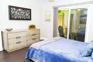 Une chambre à coucher comprenant un lit, une commode, une œuvre d’art murale et une porte-fenêtre coulissante donnant sur un espace extérieur.