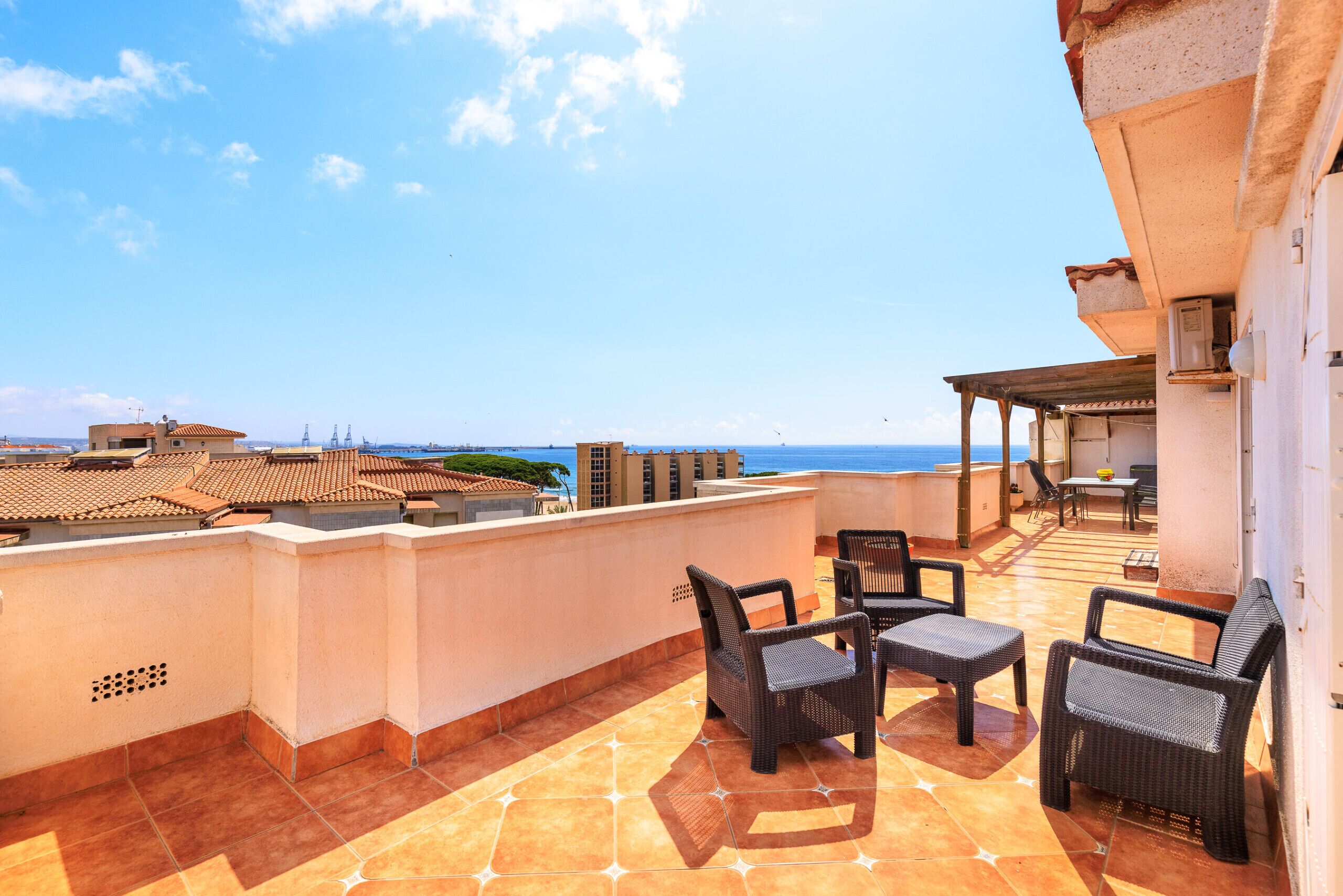 Une terrasse sur le toit, meublée de mobilier en osier, avec vue sur la mer et des bâtiments en arrière-plan.
