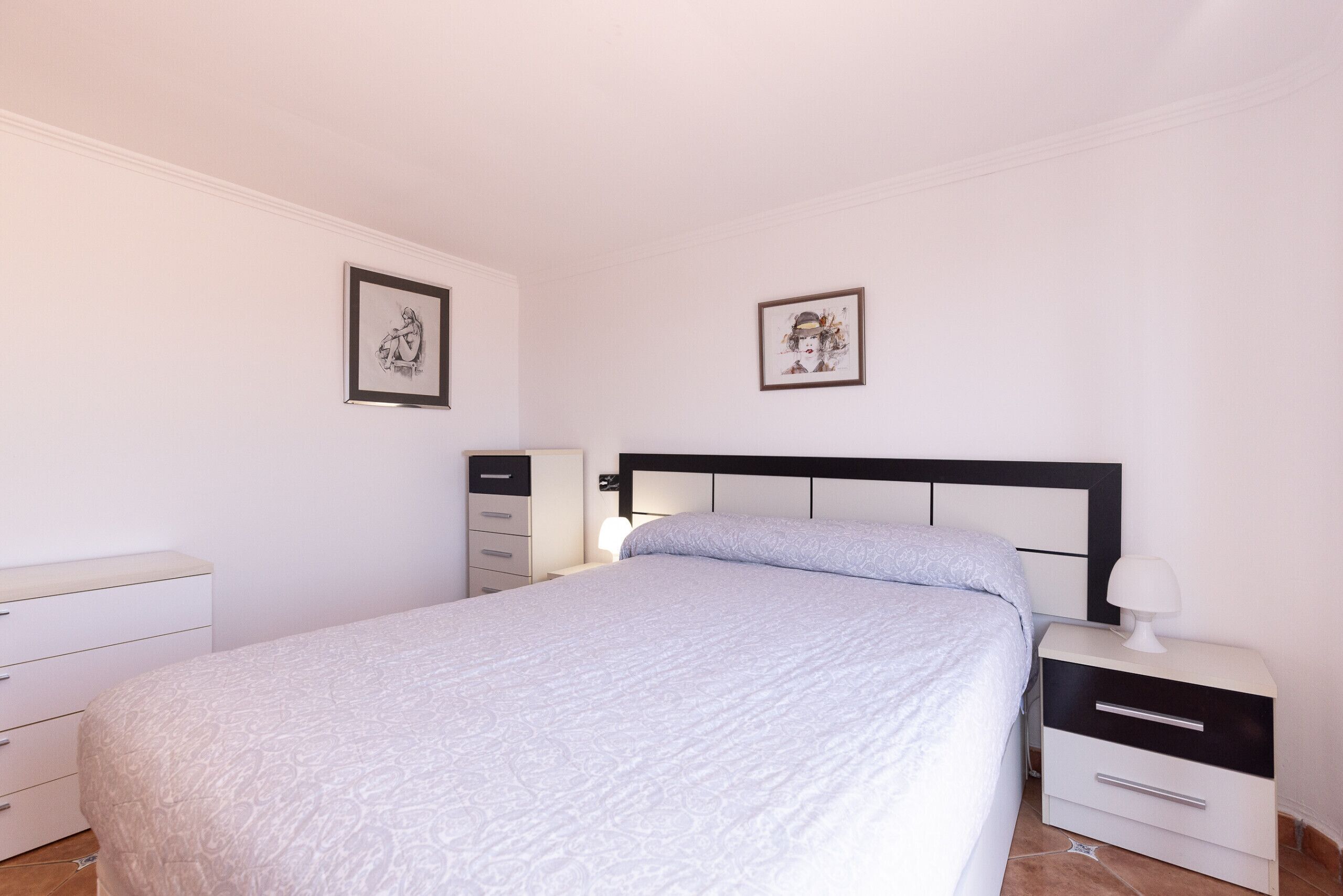 Une chambre à coucher avec un lit, une table de chevet, une commode et deux tableaux encadrés accrochés au mur.