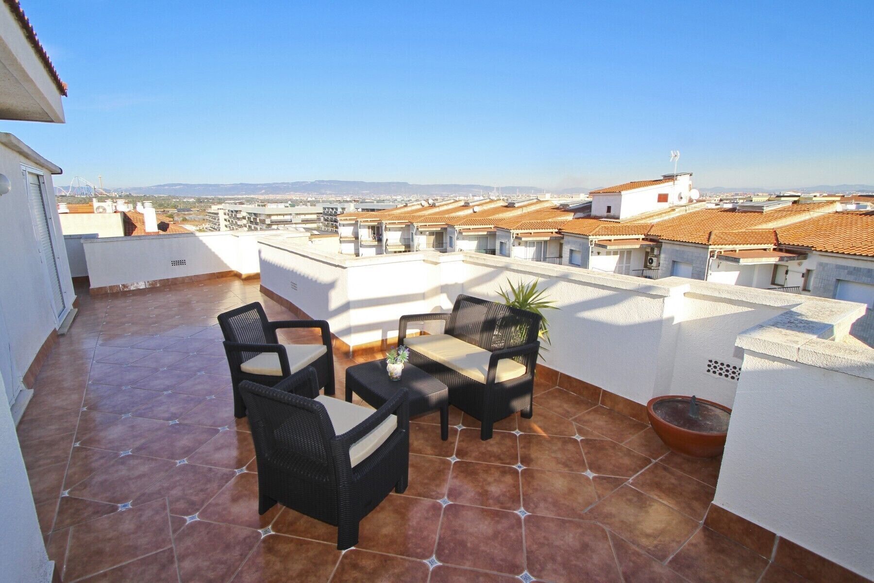 A rooftop terrace with a table and chairs, potted plants, and a view of the cityscape.