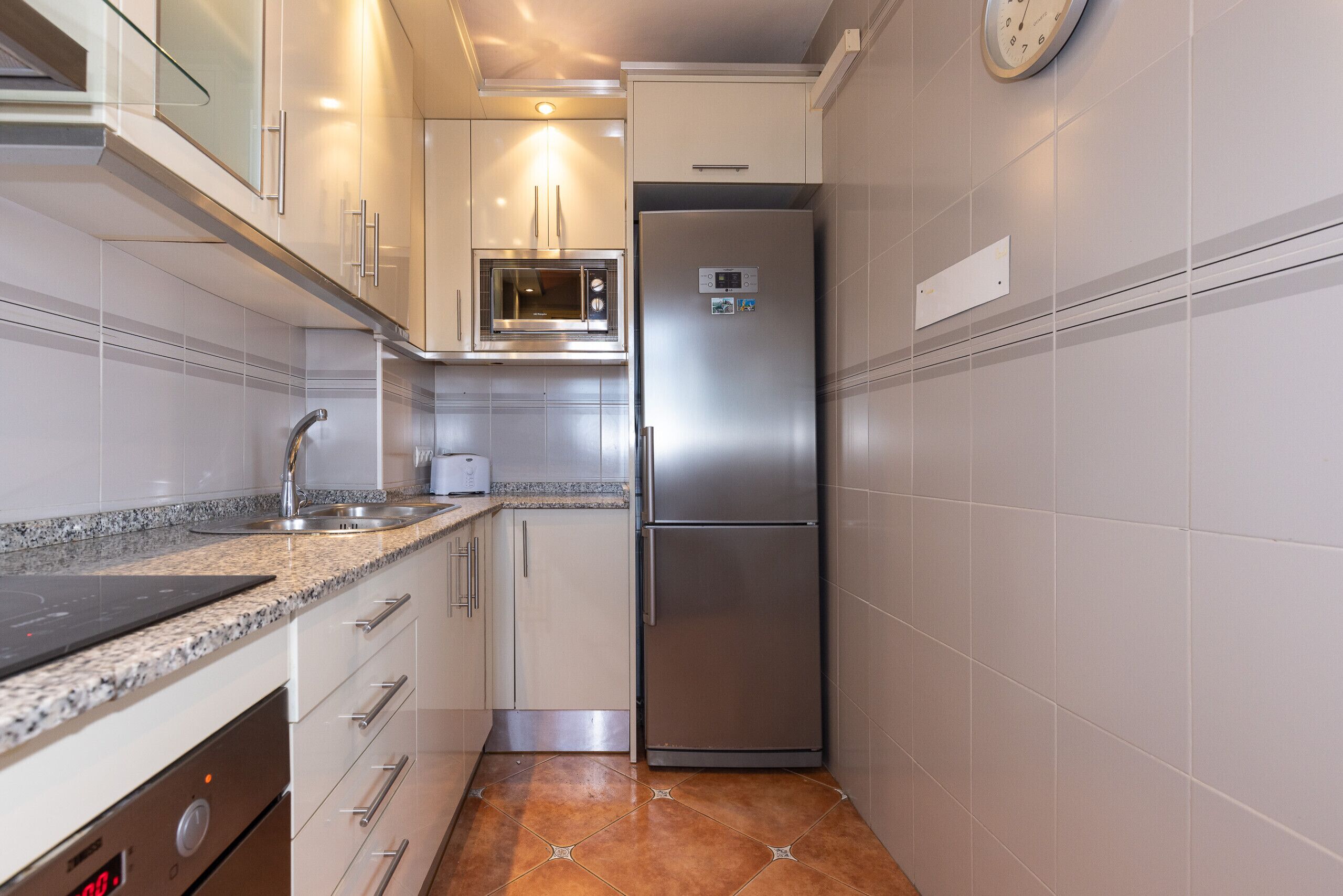 A compact kitchen with a stainless steel refrigerator, a microwave, and a built-in oven.