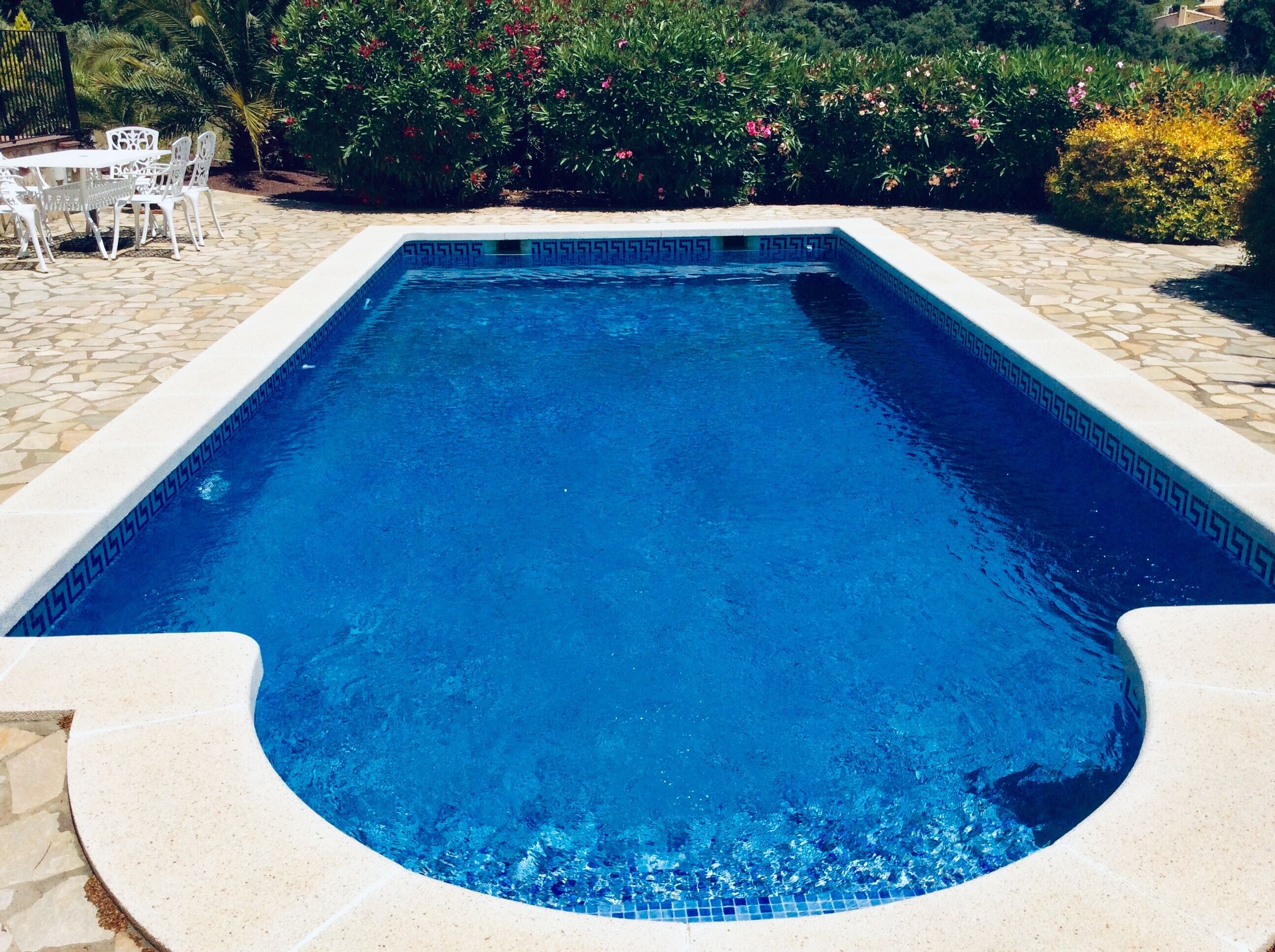Una piscina rectangular con superficie de agua azul cristalina, rodeada por un suelo de piedra y un borde decorativo.