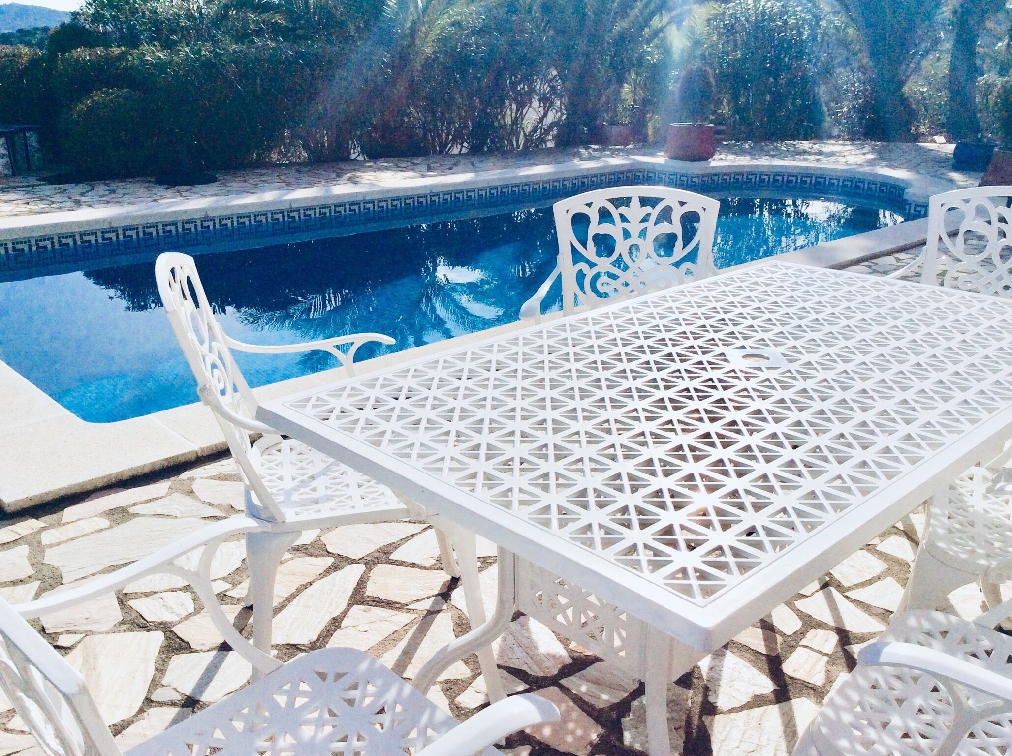 A poolside area with a white table and chairs, surrounded by stone tiles.