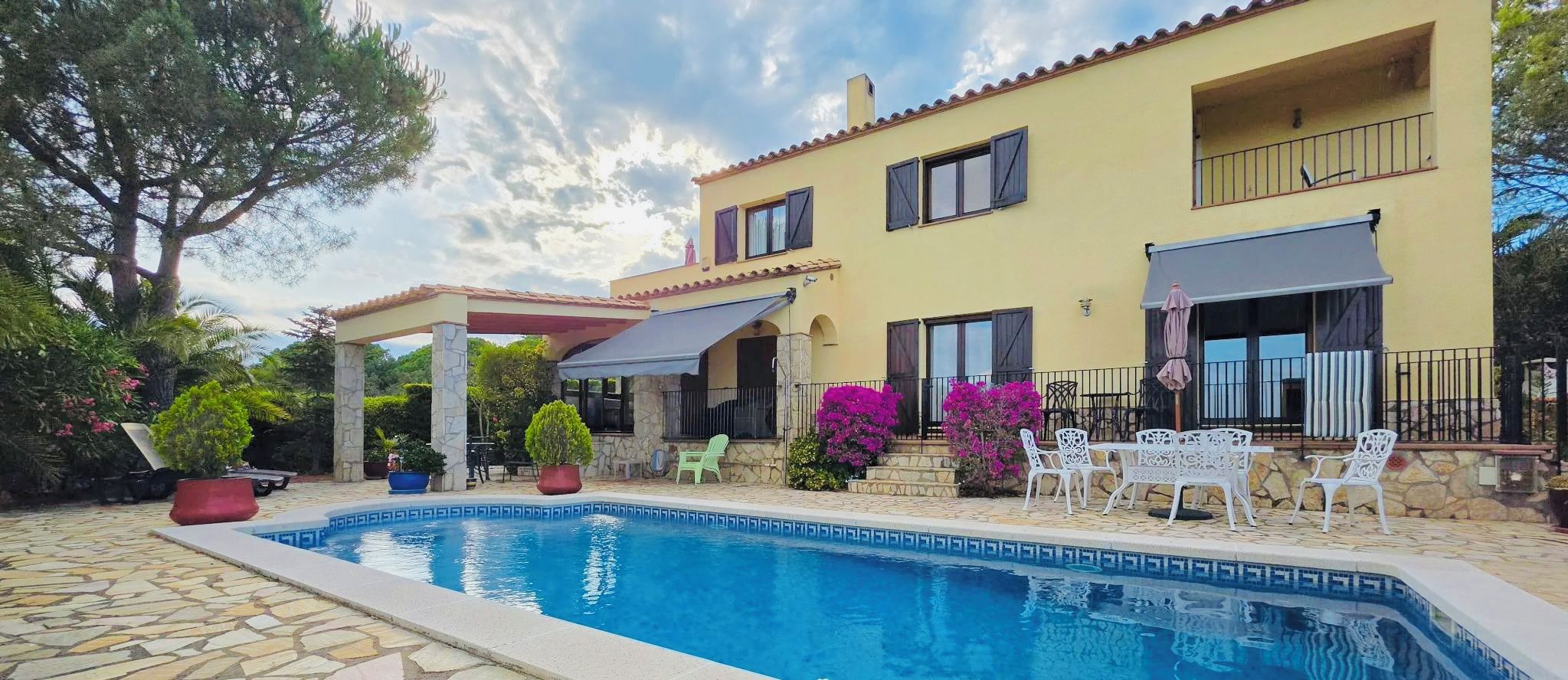 A two-story building with a swimming pool, outdoor seating, and potted plants.