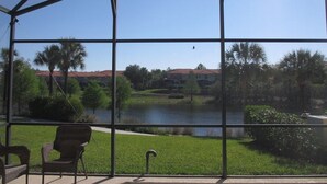 A covered outdoor area with chairs and a view of a lake, palm trees, and buildings in the background. - Amazing Lake View : 4 Bed End Townhouse : Super Fast WiFi : Private Pool (Kissimmee)