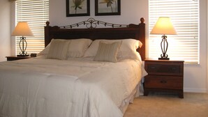 A neatly made bed with a wooden headboard, two bedside tables with lamps, and two framed pictures on the wall. - Amazing Lake View : 4 Bed End Townhouse : Super Fast WiFi : Private Pool (Kissimmee)