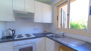 A kitchen with white cabinets, a stove, a sink, and a window with blinds. - Holiday villa with swimming pool near the Paphos coast (Paphos)