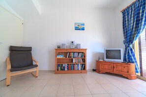 Un salon avec un canapé, une bibliothèque en bois, un téléviseur et un tableau accroché au mur.
