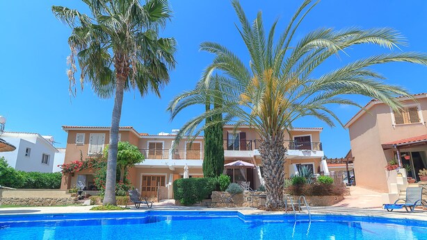 A swimming pool with lounge chairs, palm trees, and a building with balconies. - Holiday villa with swimming pool near the Paphos coast (Paphos)