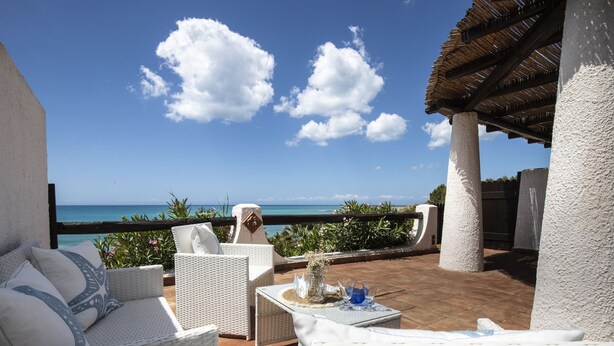 Una terrazza con mobili in vimini, un tavolo con un vaso e vista sull'oceano.