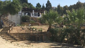 Una scala in pietra conduce a un edificio con tetto in tegole, immerso nel verde e tra palme.
