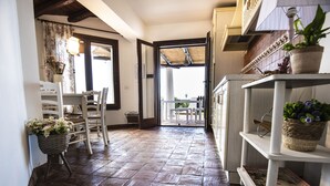 Una cucina con pavimento piastrellato, mobili bianchi e soffitto in legno. C'è un'area pranzo con tavolo e sedie, e un cesto di fiori sul pavimento.