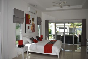 Un dormitorio con cama, mesita de noche, ventilador de techo, aire acondicionado y vistas al exterior.