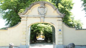 Un arc en pierre orné, surmonté d’un blason et flanqué de deux statues de lions en pierre, mène à un sentier.