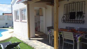 A covered outdoor dining area with a pool, a kitchen, and a patio with a table and chairs.