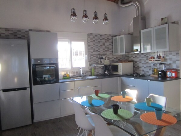 A modern kitchen with white cabinets, a refrigerator, an oven, a microwave, and a sink. There is a dining table with colorful placemats and white chairs.