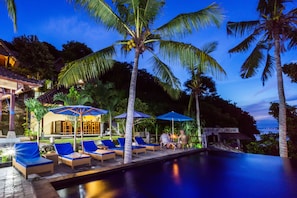 A poolside area with lounge chairs and umbrellas, surrounded by palm trees and a view of the sea. - Songlambung Beach Huts (Lembongan Island)