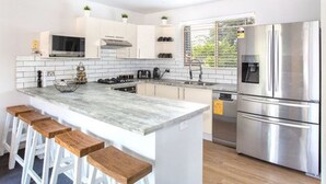 Una cocina moderna con armarios blancos, un refrigerador de acero inoxidable y una isla de mármol con taburetes de bar.