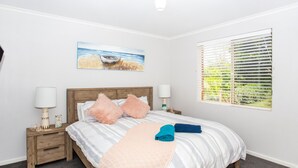 Un dormitorio con una cama, dos mesitas de noche, una lámpara auxiliar y un cuadro en la pared.
