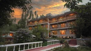 Un hotel a più piani con balconi, una facciata in pietra e un'area giardino con ringhiera bianca.