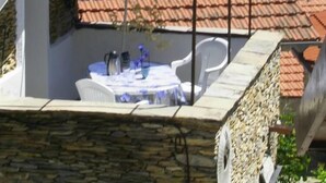 Una terraza con mesa y sillas, un paraguas azul y un muro de piedra.