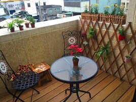 Un balcón con una mesa redonda de vidrio, dos sillas y plantas en macetas.