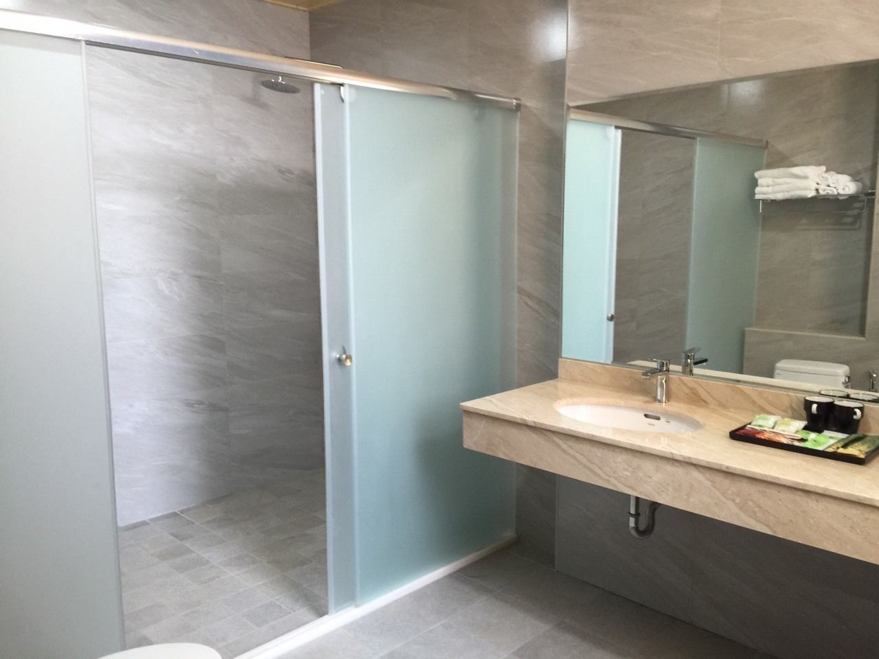 A modern bathroom with a glass shower enclosure, a marble sink, and a large mirror.