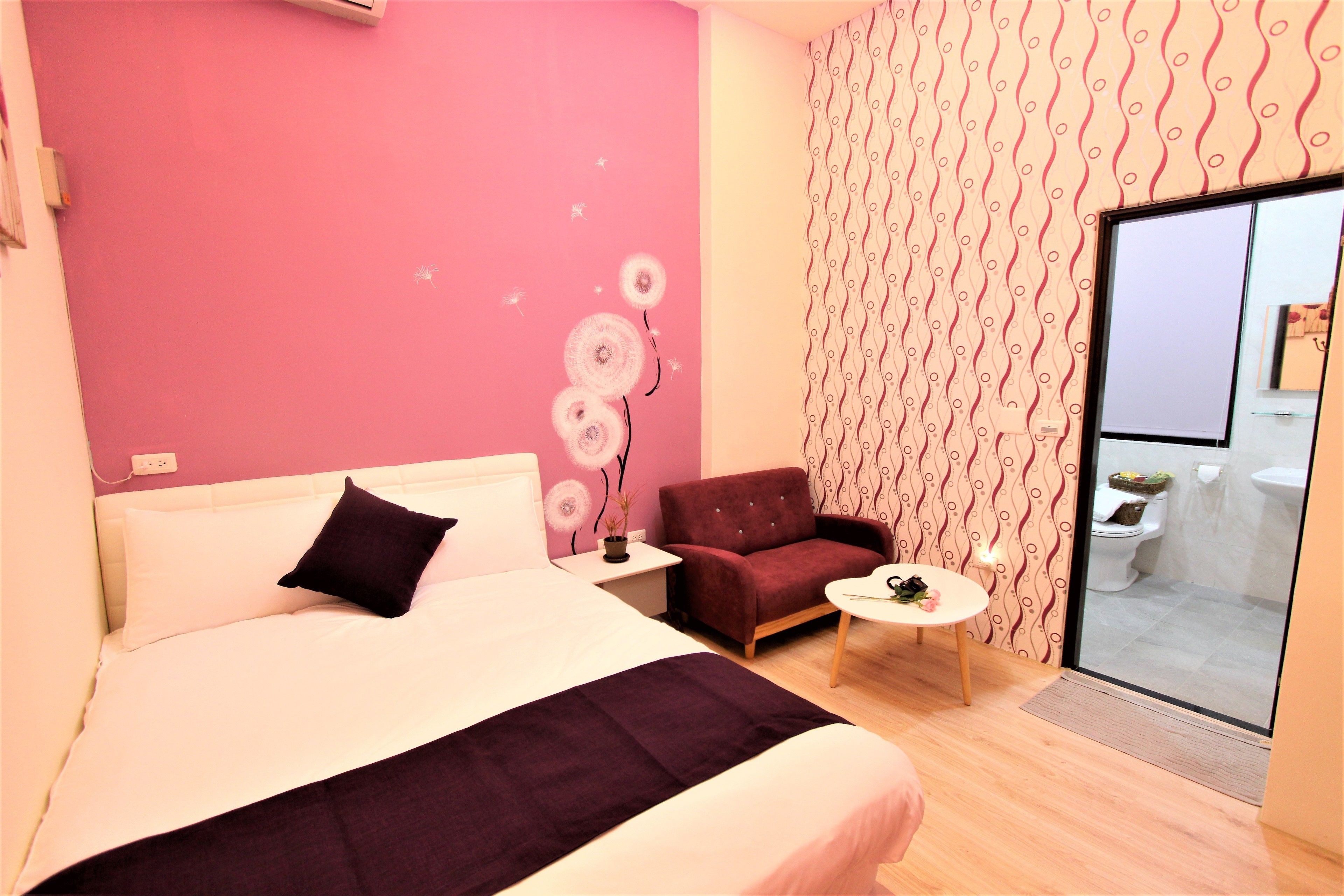 A modern bedroom with a large bed, a small table, a chair, and a view of the bathroom through a glass door.