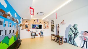 Una habitación con televisión, una banca, una mesita pequeña y un mural en la pared.