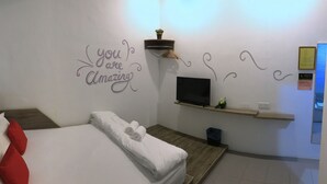 Habitación de hotel con cama, televisor, estante en la pared y una frase motivacional.